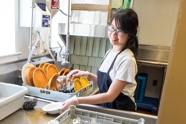 A student washing dishes in a house dining room.