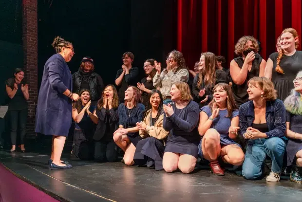 A group of students on the stage in Mendenhall, clapping and smiling as Sarah Willie-LeBreton greets them